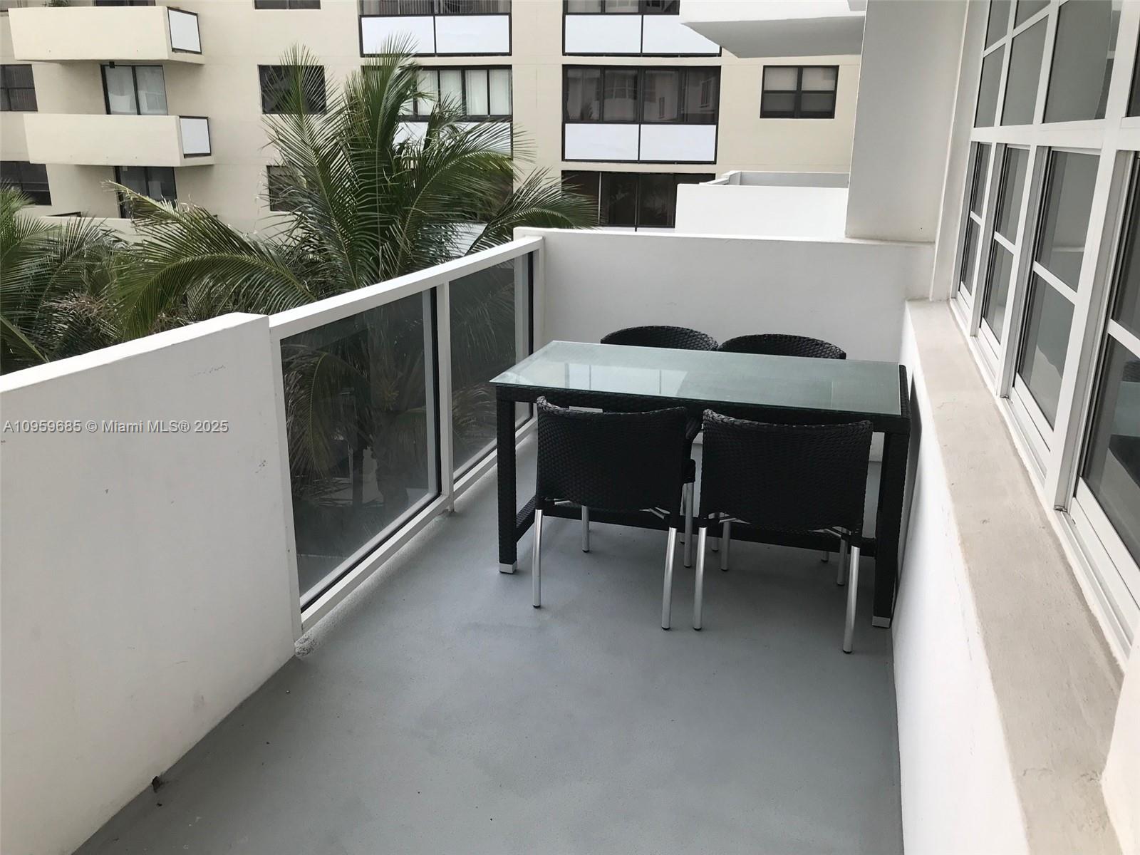 A balcony features a glass-topped table with four black wicker chairs and a glass railing — 100 Lincoln Rd # 719, Miami Beach FL 33139, MIAMI BEACH, FL