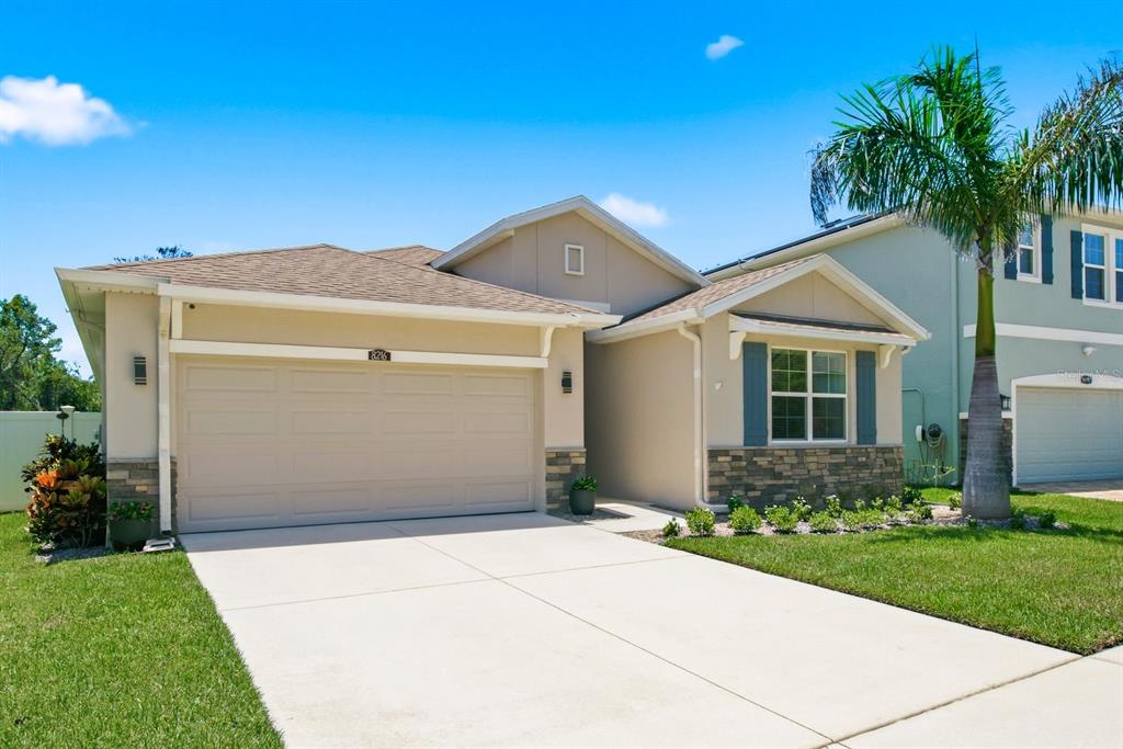 A single-story suburban house with a tan stucco exterior, stone accents, and a two-car garage — 8216 PRAISE DRIVE, TAMPA, FL