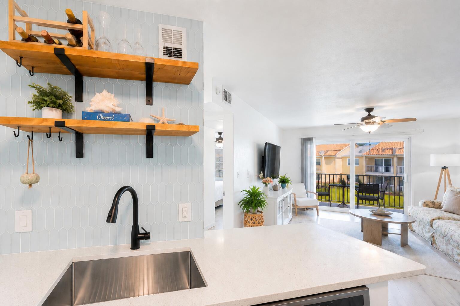 A kitchen sink and open shelving overlook a living room with a balcony view — 1850 Charlesmont Drive # 119, Indialantic FL 32903, INDIALANTIC, FL