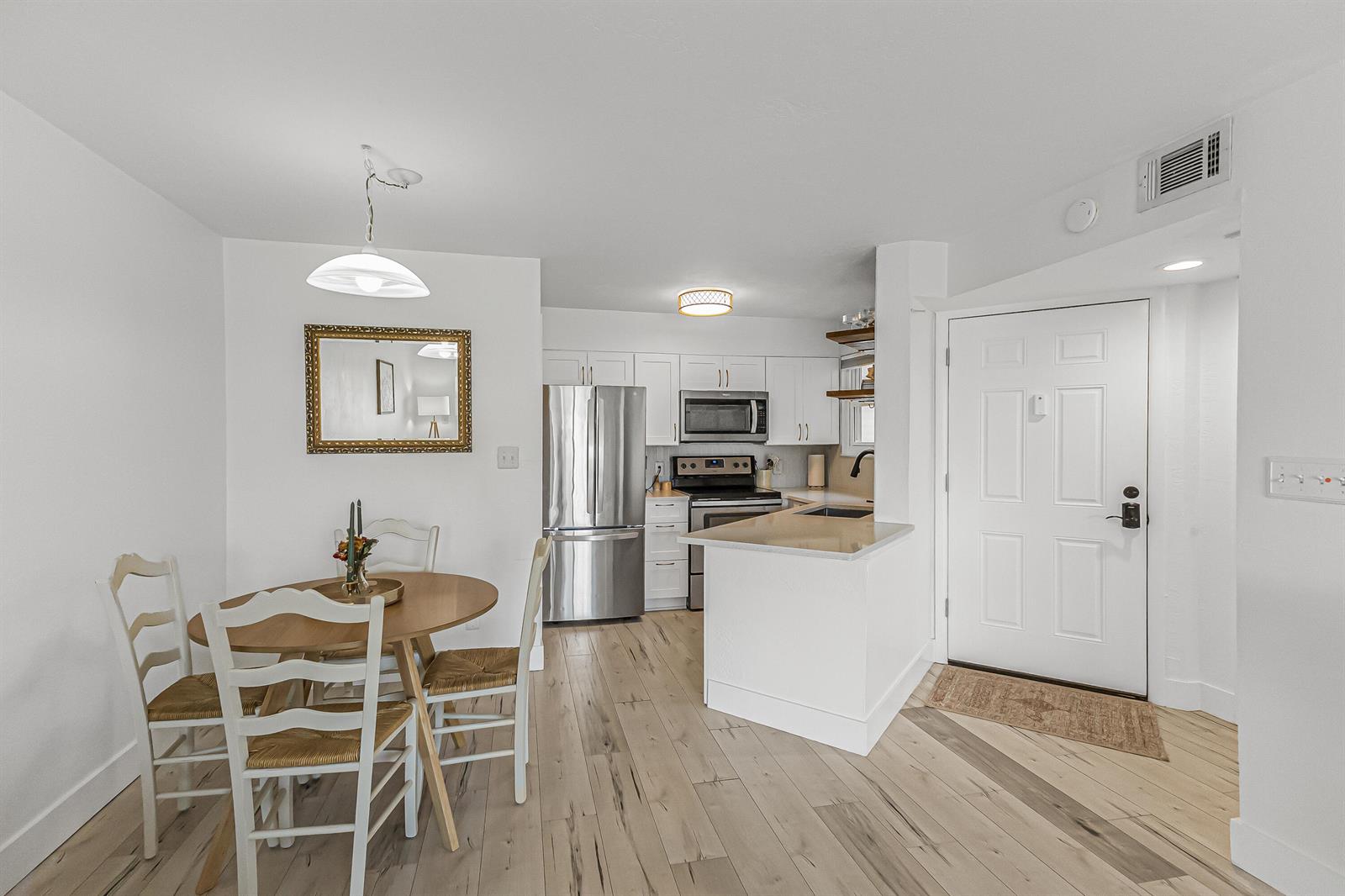 A dining area with a round table and chairs sits adjacent to a white kitchen — 1850 Charlesmont Drive # 119, Indialantic FL 32903, INDIALANTIC, FL