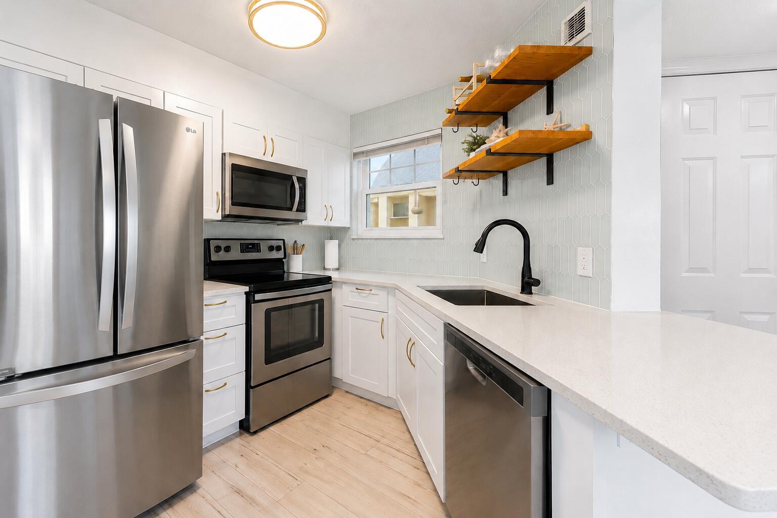 A kitchen with white cabinets, stainless steel appliances, light wood floors, and open wooden shelving — 1850 Charlesmont Drive # 119, Indialantic FL 32903, INDIALANTIC, FL