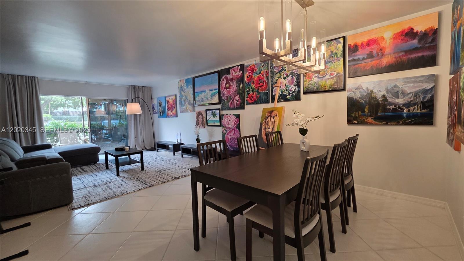 A dining and living area features tile floors, a dark wood table, and many wall paintings — 3360 Spanish Moss Ter # 104, Lauderhill FL 33319, LAUDERHILL, FL
