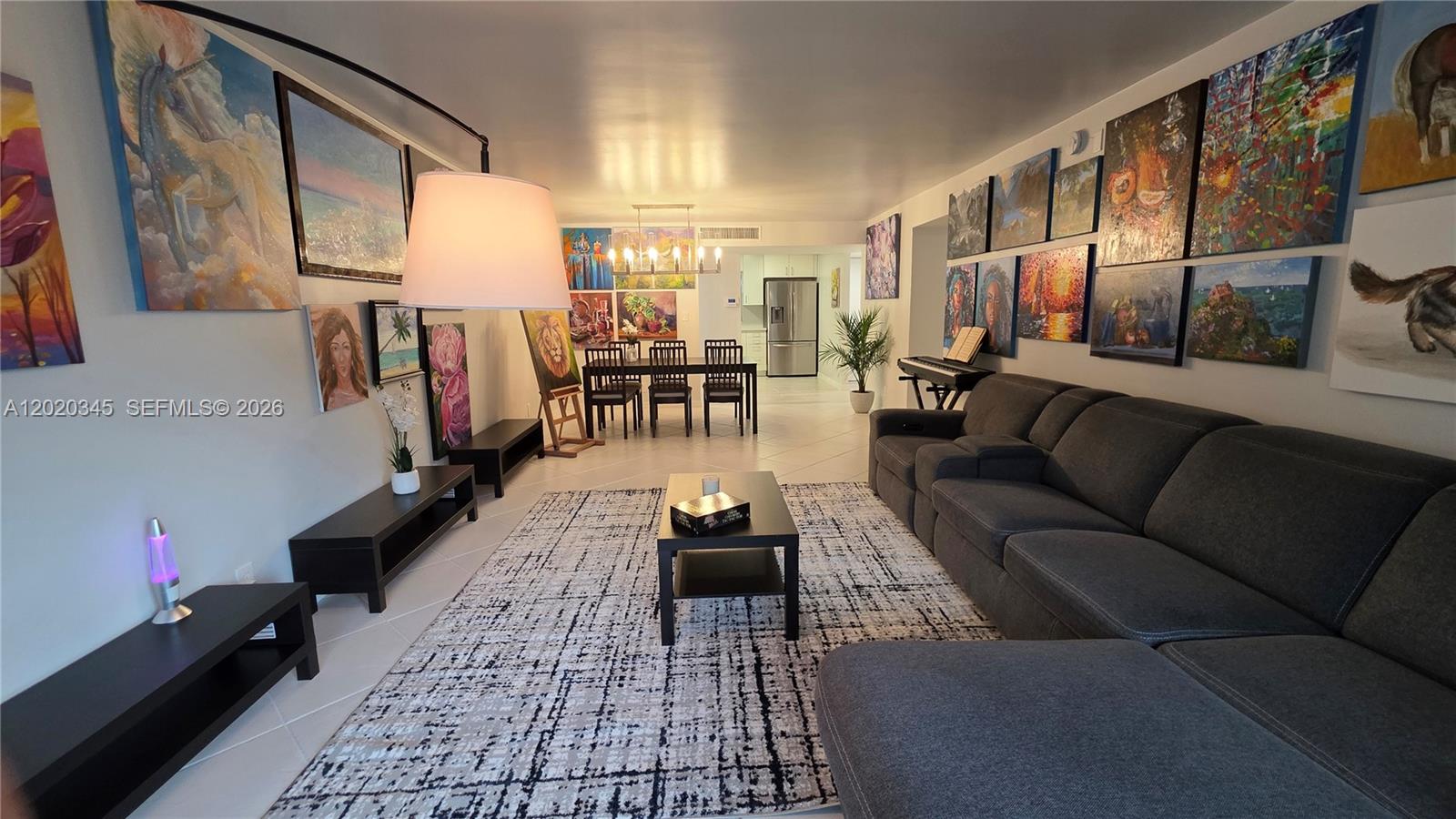 A living room features a large gray sectional sofa, a patterned rug, and numerous wall paintings — 3360 Spanish Moss Ter # 104, Lauderhill FL 33319, LAUDERHILL, FL