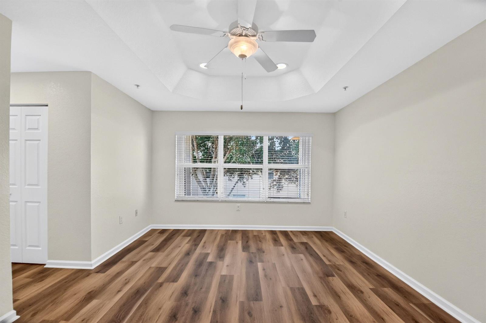 An empty room with wood-look flooring, a tray ceiling, a ceiling fan, and a window — 7662 Spatterdock Drive, Boynton Beach FL 33437, BOYNTON BEACH, FL