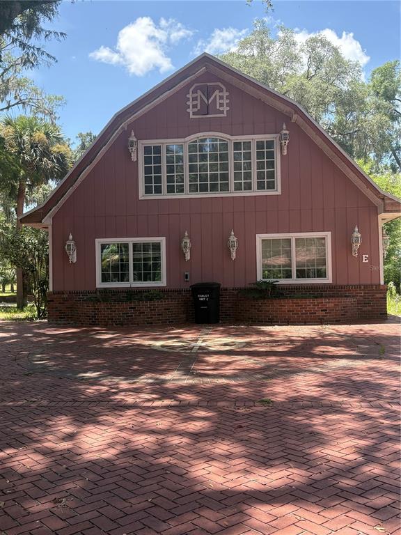 A two-story barn-style building with a brick base, red siding, and a circular brick driveway — 976 SW HAMLET CIRCLE UNIT E, LAKE CITY, FL
