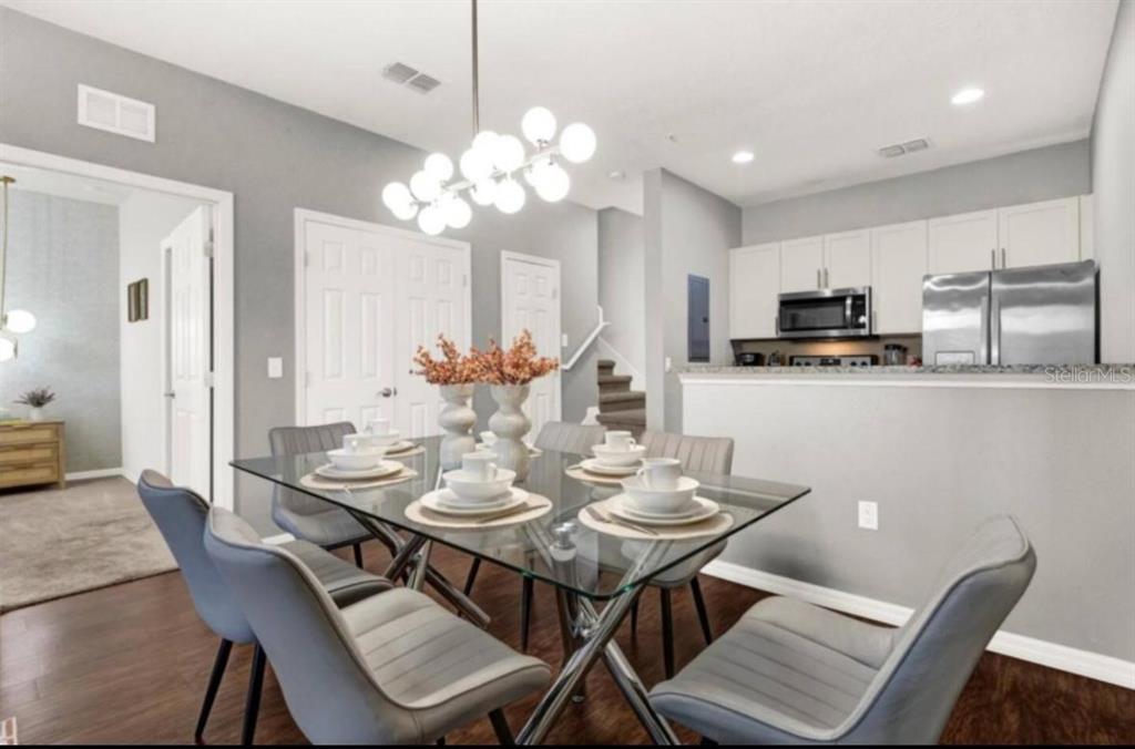 A dining area with a glass table, gray chairs, and a modern chandelier near a kitchen — 3202 GUANA WAY, KISSIMMEE, FL