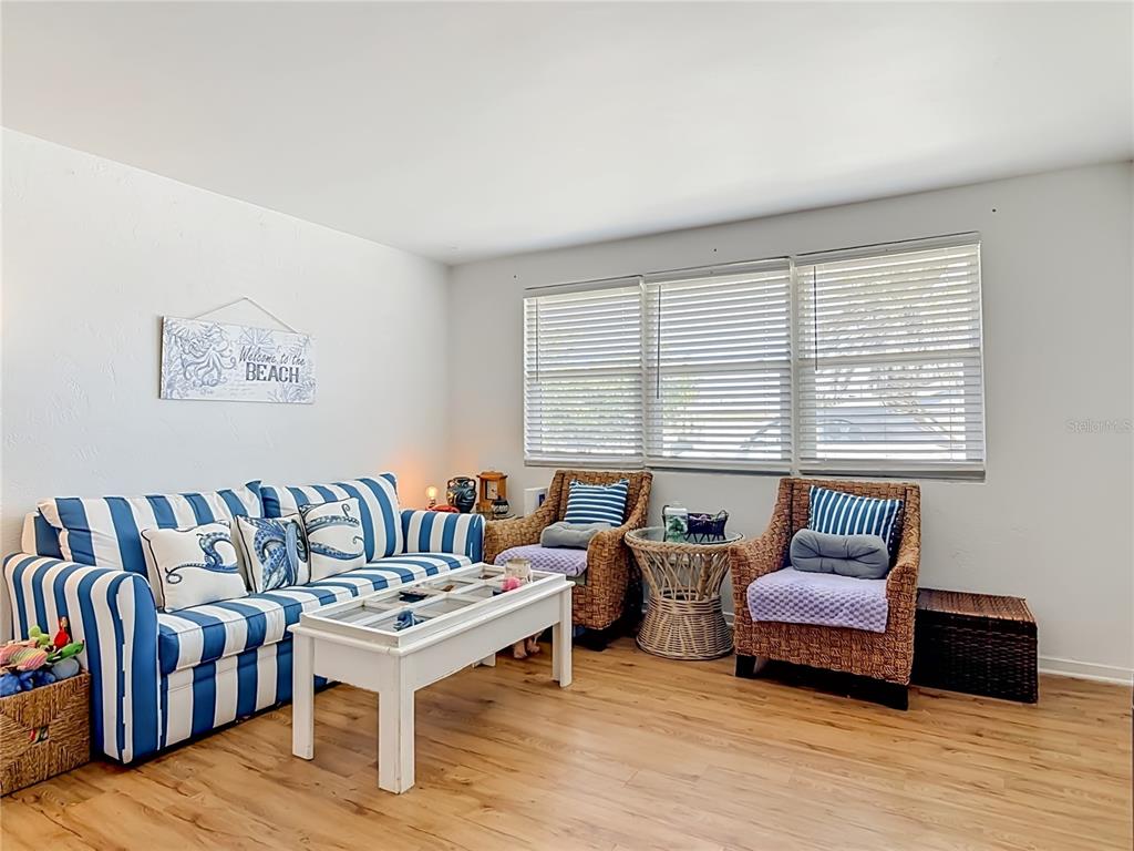 A living room features a blue and white striped sofa, wicker chairs, and wood flooring — 27 ALAMANDA DRIVE, ORMOND BEACH, FL