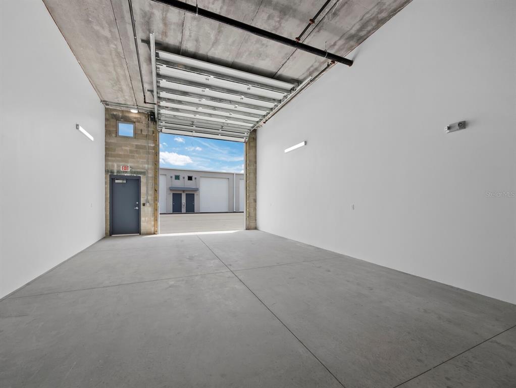 An industrial warehouse space with a concrete floor, white walls, and an open roll-up door — 829 57TH STREET E UNIT 28, BRADENTON, FL