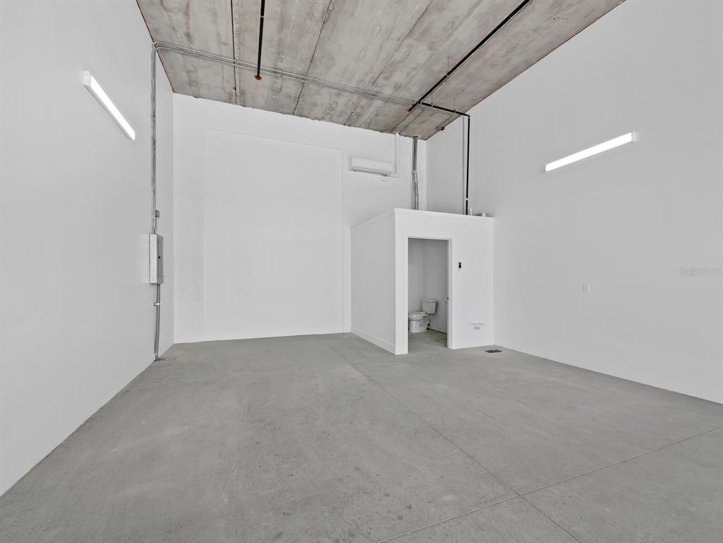 An industrial-style room with concrete floors, high ceilings, and a small enclosed restroom — 829 57TH STREET E UNIT 28, BRADENTON, FL