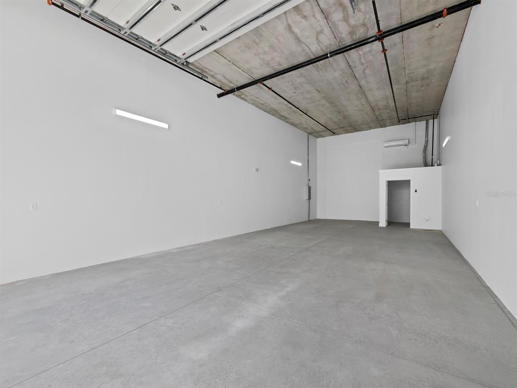 An empty industrial warehouse space with concrete floors, white walls, and exposed ceiling pipes — 829 57TH STREET E UNIT 28, BRADENTON, FL