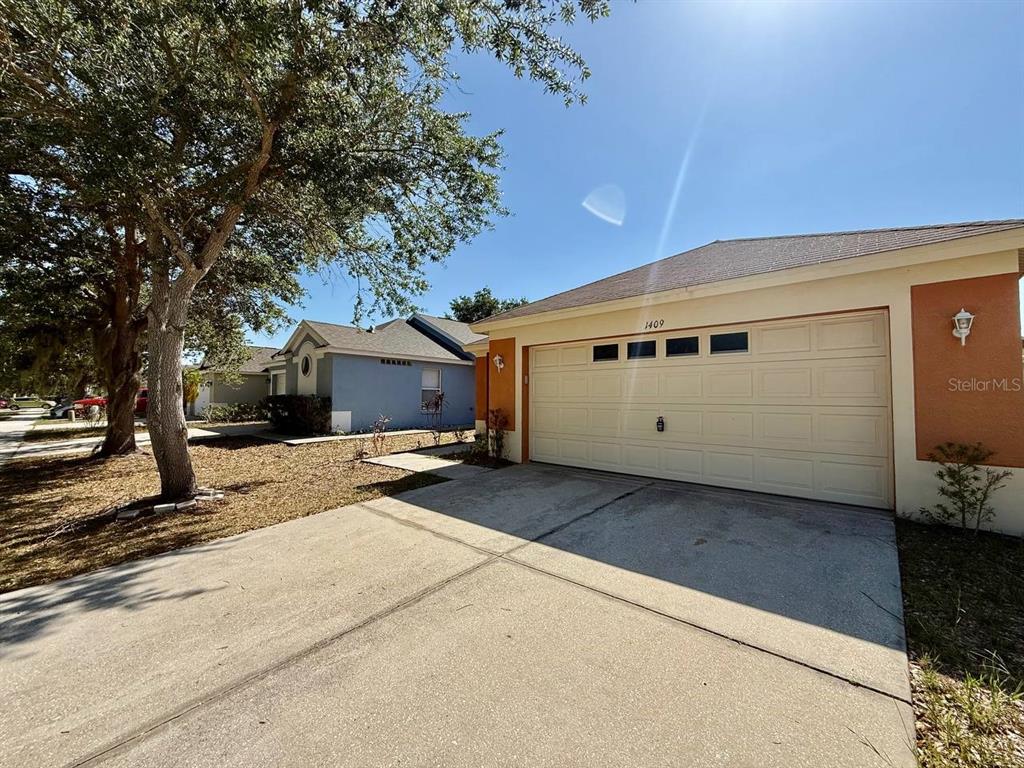 A single-story house with a beige garage door and orange exterior accents under a clear sky — 1409 DELANO TRENT STREET, RUSKIN, FL