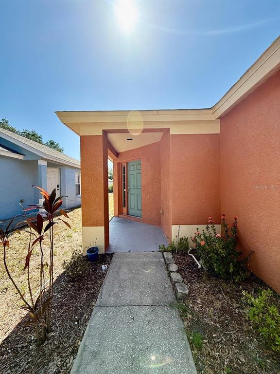 A concrete walkway leads to the recessed front entrance of an orange stucco house — 1409 DELANO TRENT STREET, RUSKIN, FL