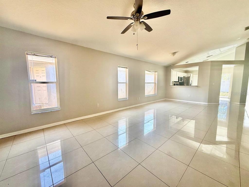 An empty living room features light-colored tile flooring, a ceiling fan, and three windows — 1409 DELANO TRENT STREET, RUSKIN, FL