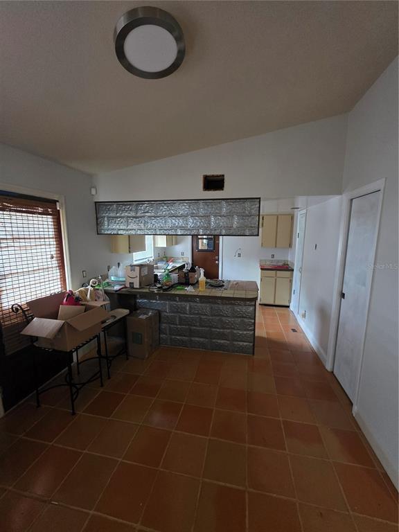 A kitchen features a metal-paneled breakfast bar, terracotta-colored floor tiles, and light-colored cabinetry — 9387 JUNIOR AVENUE, APOPKA, FL