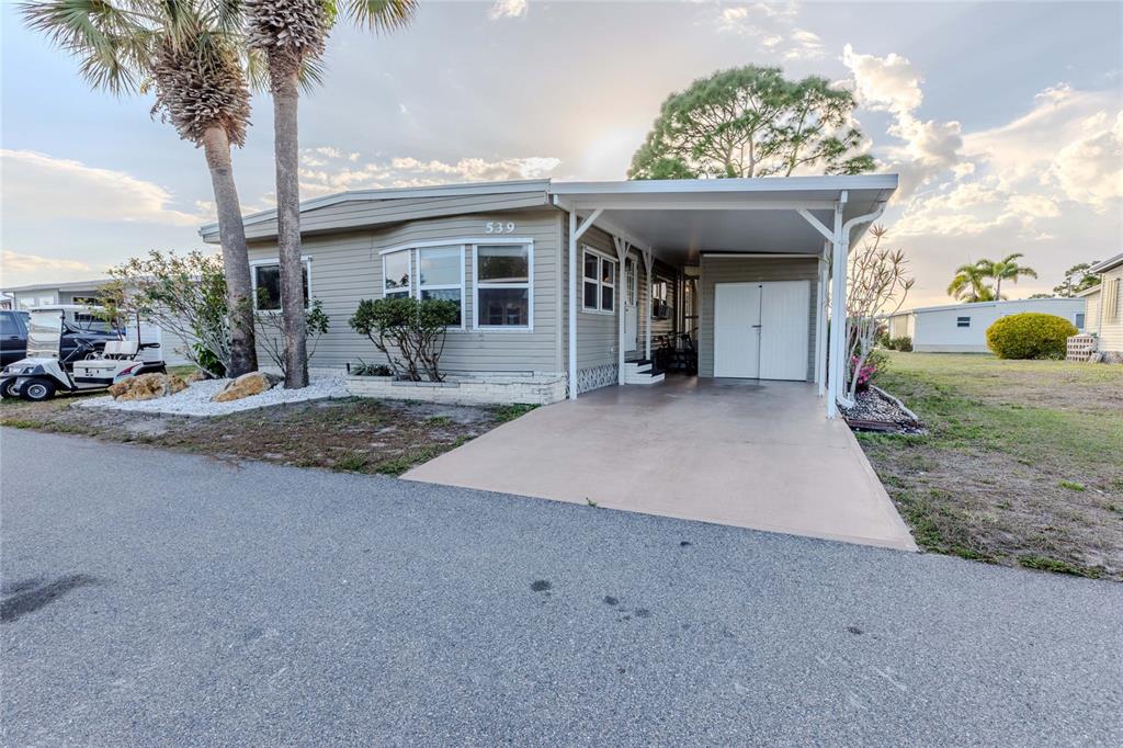 A single-story manufactured home with a carport, palm trees, and a paved driveway — 2100 KINGS HIGHWAY UNIT 539, PORT CHARLOTTE, FL
