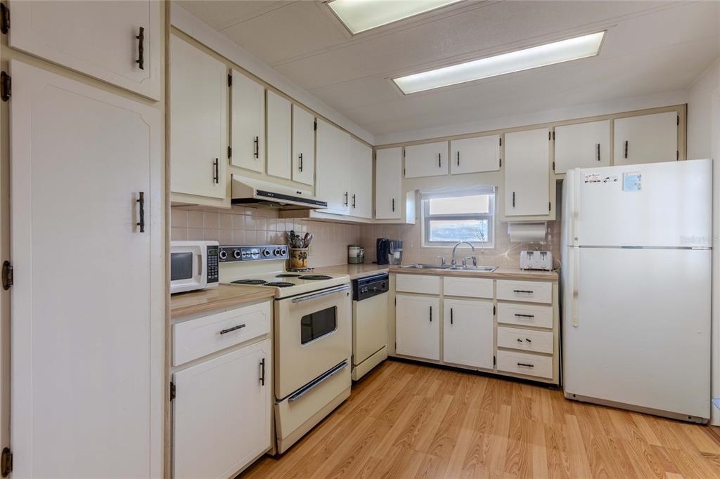 A kitchen features white cabinets, light wood-look flooring, a white stove, and a white refrigerator — 2100 KINGS HIGHWAY UNIT 539, PORT CHARLOTTE, FL