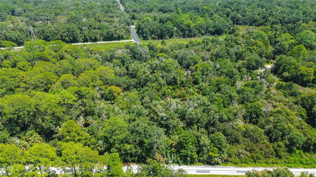 An aerial view shows a densely wooded lot bordering a paved road and intersection — 8683 N BELLFLOWER WAY, CRYSTAL RIVER, FL