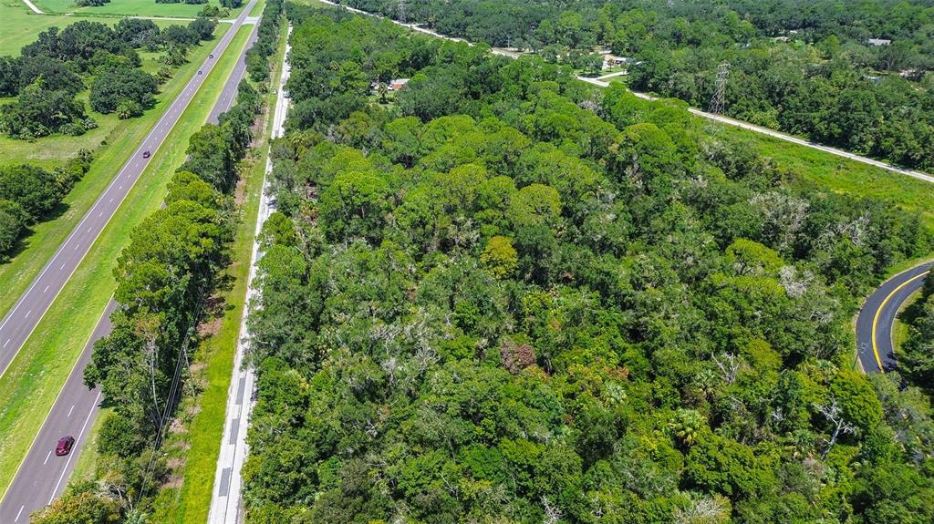 An aerial view shows a dense wooded lot bordered by a highway and a curved road — 8683 N BELLFLOWER WAY, CRYSTAL RIVER, FL