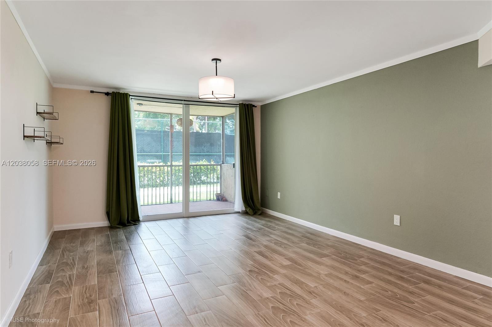 An empty living room features wood-look tile floors, a green accent wall, and sliding glass doors — 8205 Lake Dr # 103, Doral FL 33166, DORAL, FL