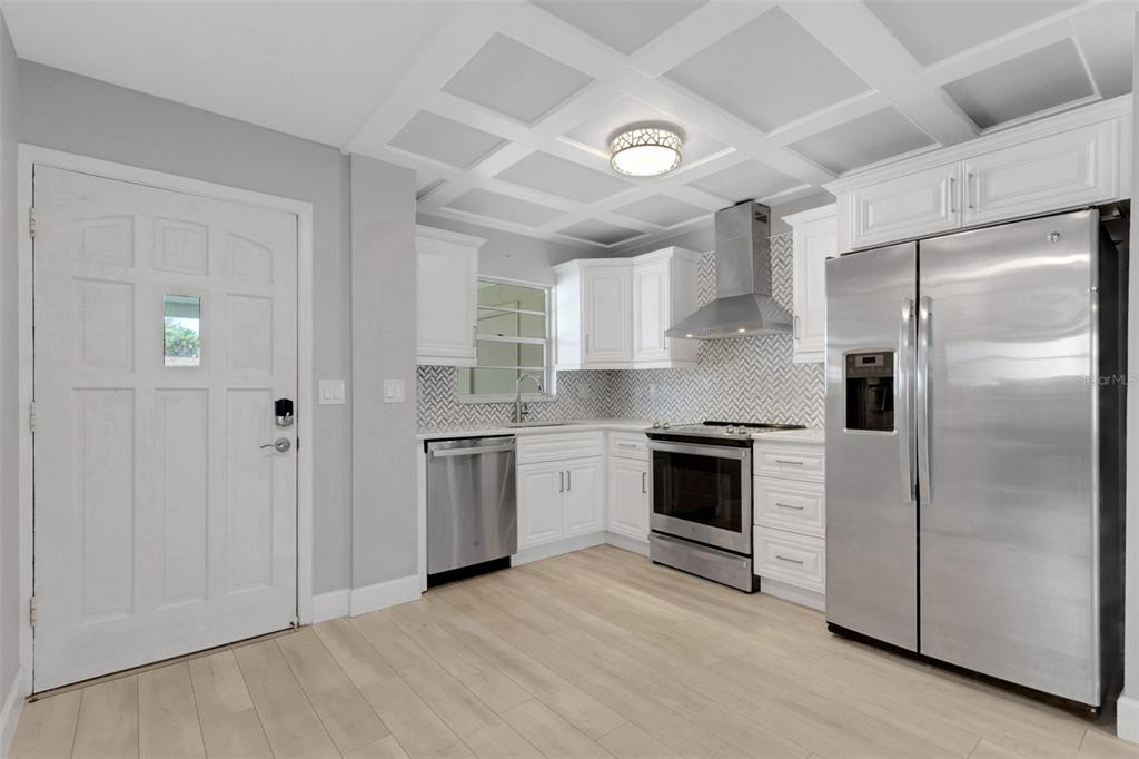 A kitchen features white cabinets, stainless steel appliances, a herringbone backsplash, and a coffered ceiling — 4602 PARK ACRES DRIVE UNIT 96, BRADENTON, FL