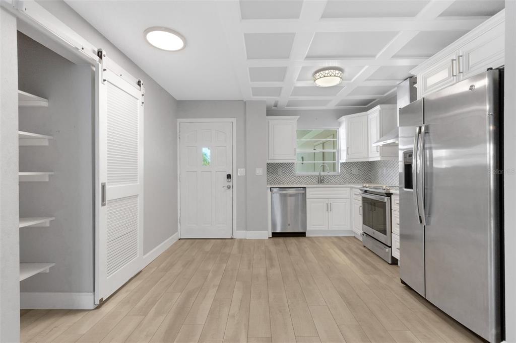A modern kitchen features white cabinetry, stainless steel appliances, light wood flooring, and a coffered ceiling — 4602 PARK ACRES DRIVE UNIT 96, BRADENTON, FL
