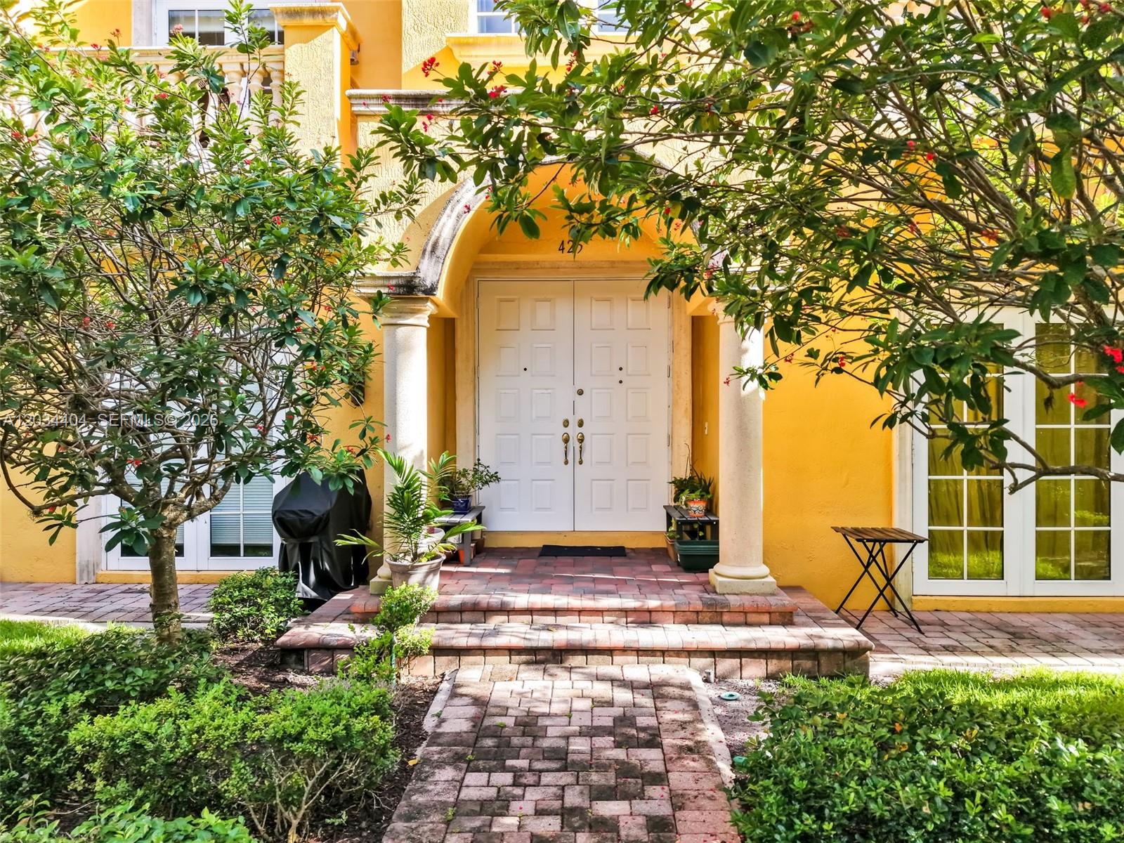 A yellow house exterior features a brick walkway leading to a double-door entryway with columns — 425 NE 69th Cir, Boca Raton FL 33487, BOCA RATON, FL