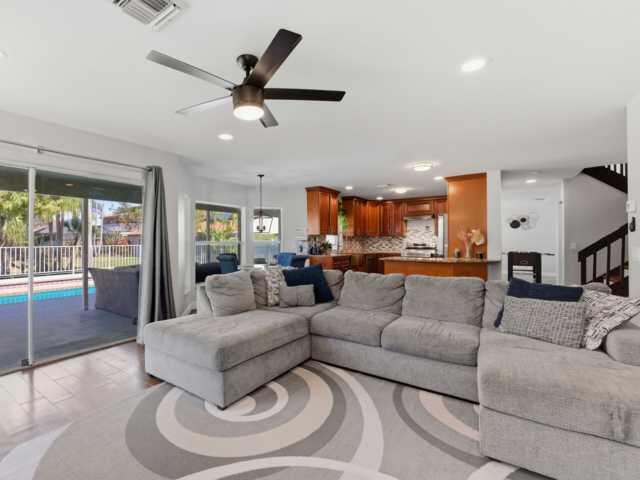 A living room with a gray sectional sofa, ceiling fan, and open kitchen with wood cabinets — 5528 Descartes Circle, Boynton Beach FL 33472, BOYNTON BEACH, FL