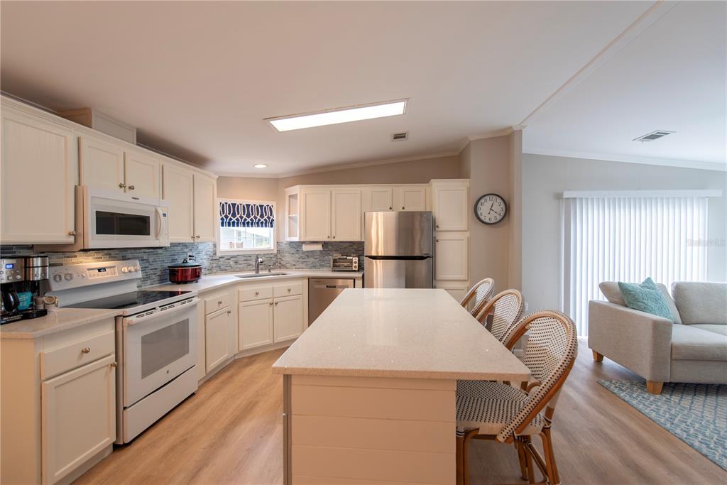 A kitchen features white cabinets, stainless steel appliances, a quartz island, and light wood flooring — 21 AMSTERDAM AVENUE, PUNTA GORDA, FL