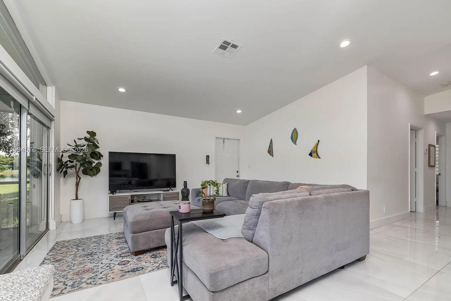 A living room features a gray sectional sofa, a television, and large sliding glass doors — 518 Woodgate Cir, Sunrise FL 33326, SUNRISE, FL