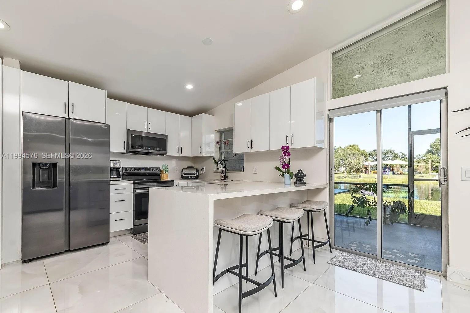 A modern kitchen features white cabinets, stainless steel appliances, a waterfall island, and sliding glass doors — 518 Woodgate Cir, Sunrise FL 33326, SUNRISE, FL