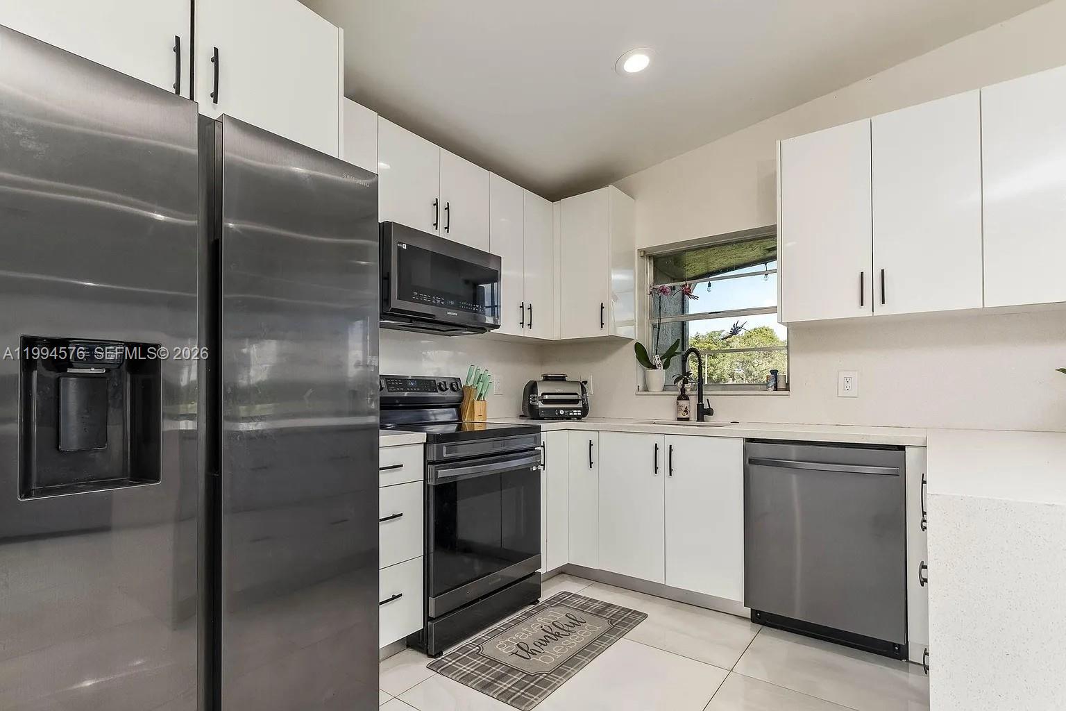 A modern kitchen features white cabinets, stainless steel appliances, and light-colored tile flooring — 518 Woodgate Cir, Sunrise FL 33326, SUNRISE, FL