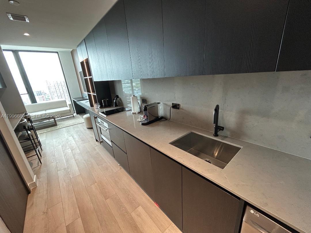 A modern kitchen features dark cabinetry, light stone countertops, and a stainless steel sink — 20 NE 11 st # 3301, Miami FL 33132, MIAMI, FL