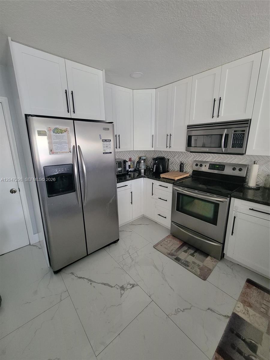 A kitchen features white cabinets, stainless steel appliances, and light-colored marble-patterned tile flooring — 6606 Saltaire Ter, Margate FL 33063, MARGATE, FL