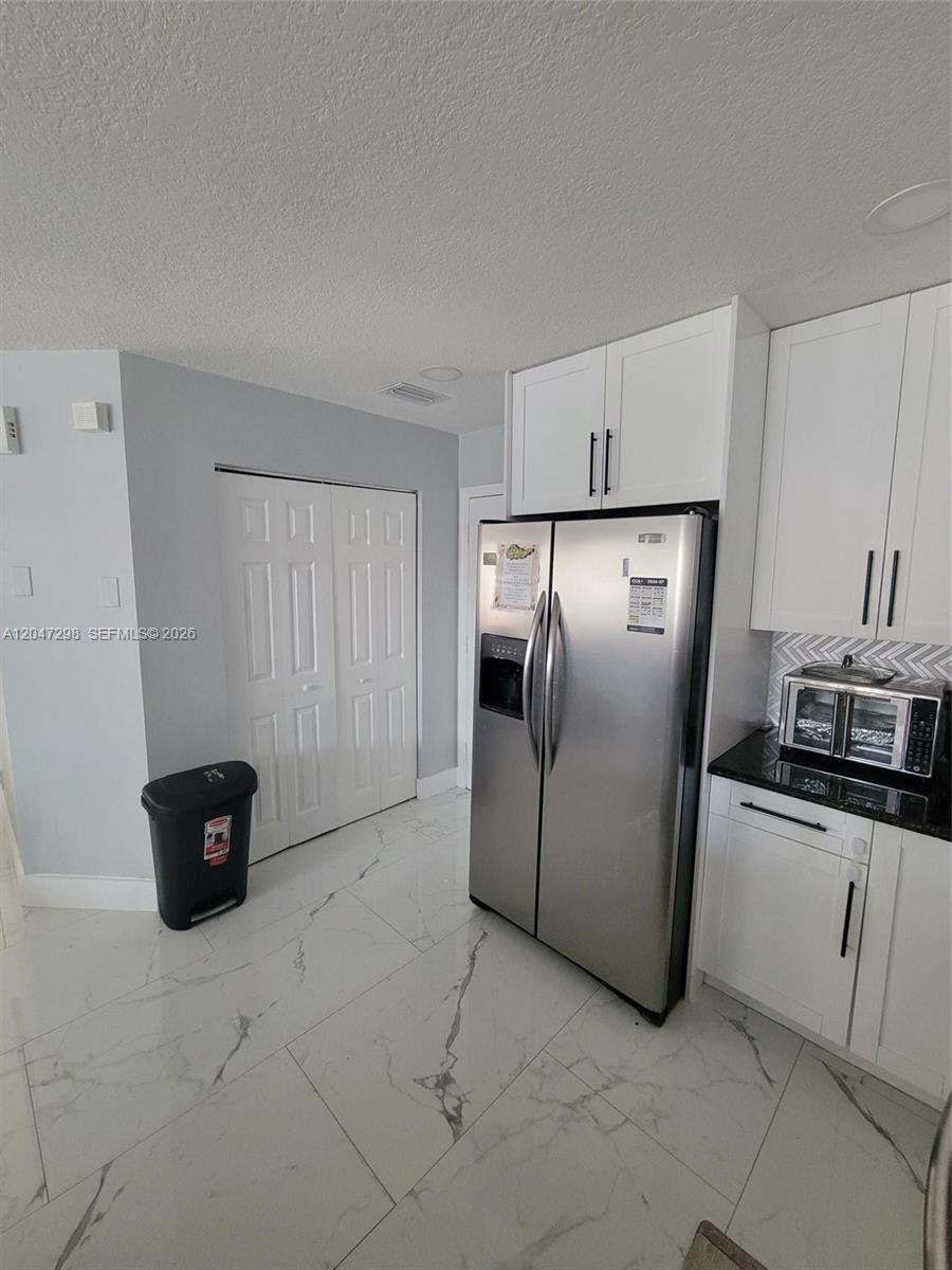 A kitchen features white cabinets, stainless steel appliances, and white marble-patterned tile flooring — 6606 Saltaire Ter, Margate FL 33063, MARGATE, FL