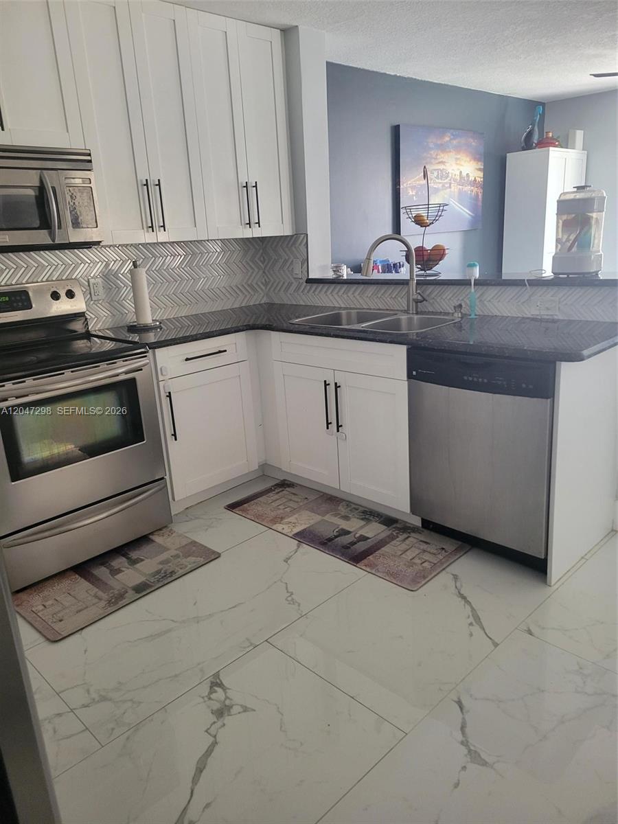A kitchen features white cabinets, stainless steel appliances, dark countertops, and a herringbone tile backsplash — 6606 Saltaire Ter, Margate FL 33063, MARGATE, FL