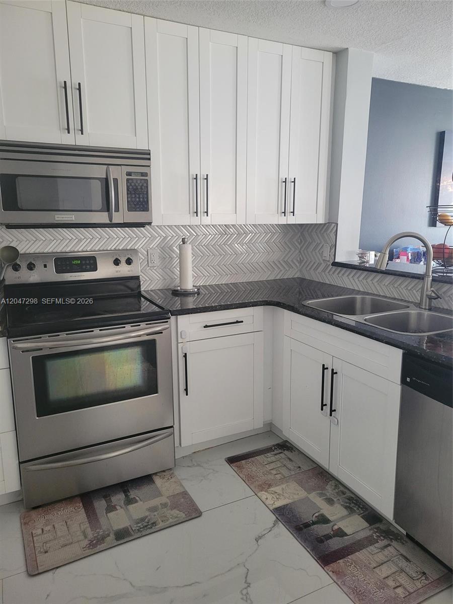 A kitchen features white shaker cabinets, stainless steel appliances, dark countertops, and a herringbone backsplash — 6606 Saltaire Ter, Margate FL 33063, MARGATE, FL