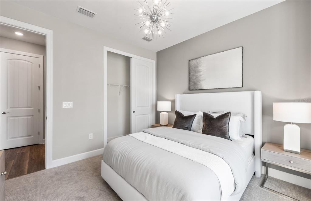 A bedroom features a white upholstered bed, gray walls, a starburst chandelier, and carpeted flooring — 26637 BERING DRIVE, ENGLEWOOD, FL