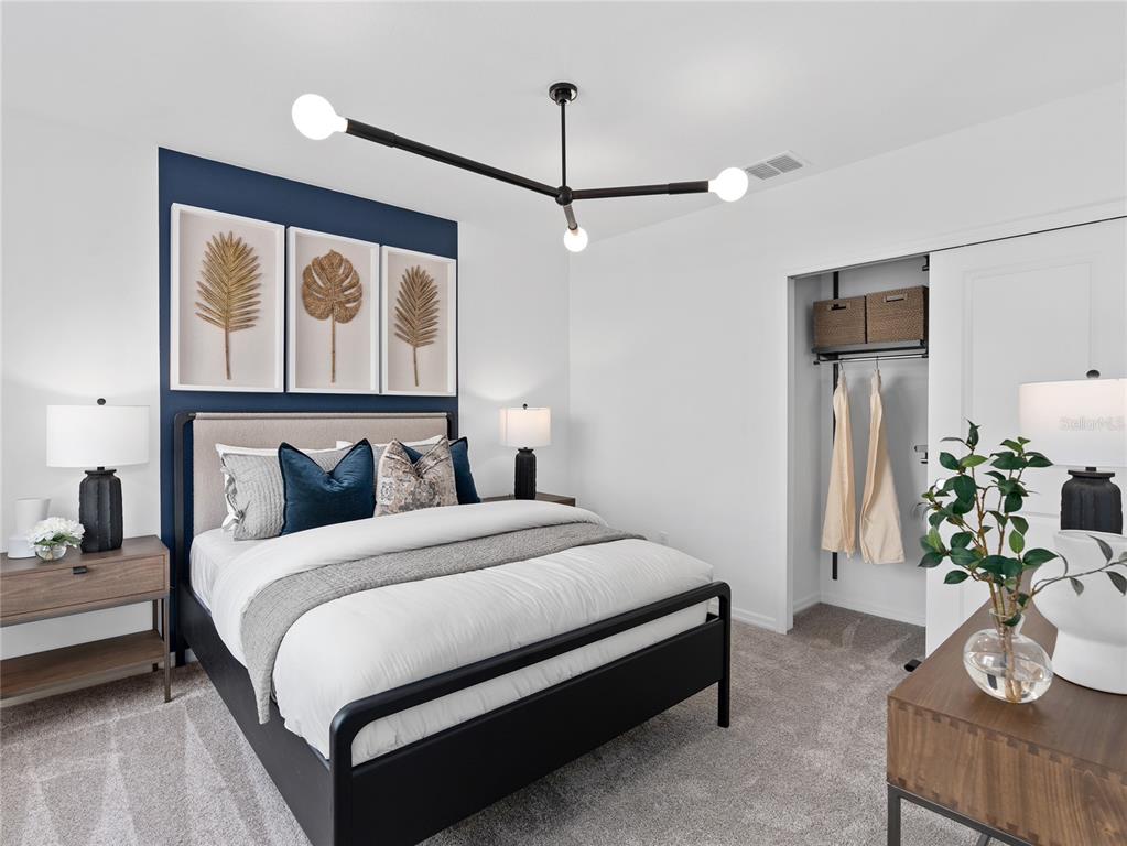 A bedroom features a navy accent wall, a black metal bed frame, and a modern chandelier — 10704 LEAFY LAUREL STREET, ORLANDO, FL