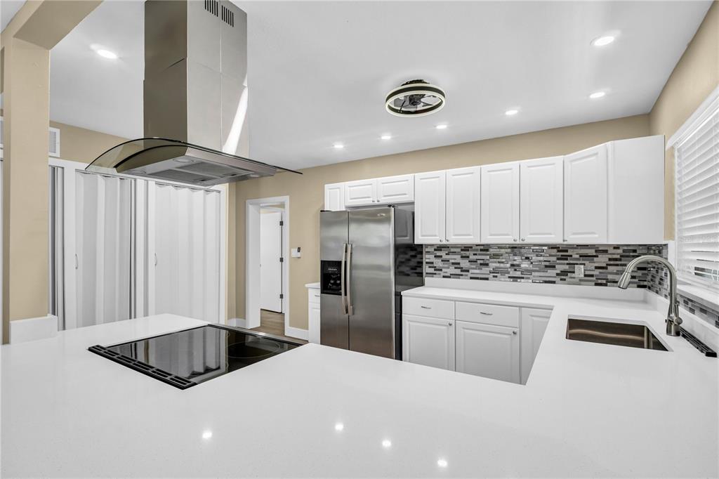A modern kitchen features white cabinets, stainless steel appliances, and a large white countertop island — 1001 JASMINE WAY, CLEARWATER, FL