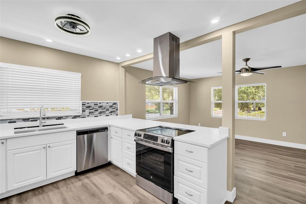 A modern kitchen features white cabinets, stainless steel appliances, and a central range hood — 1001 JASMINE WAY, CLEARWATER, FL