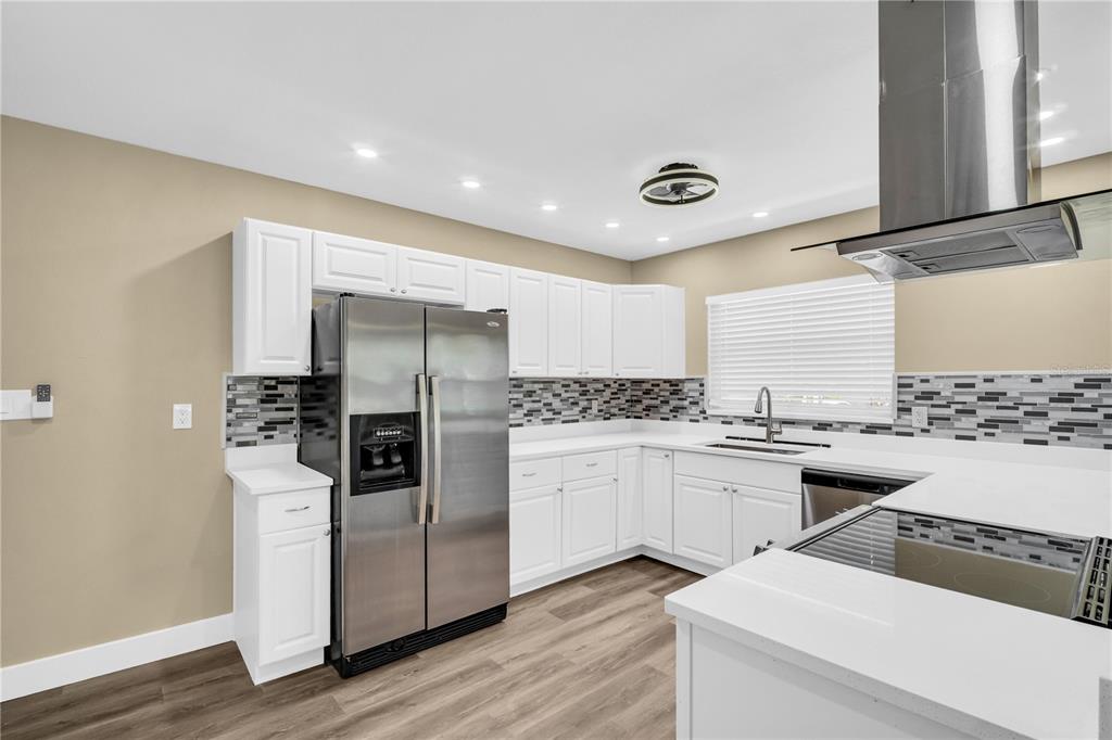 A kitchen with white cabinets, stainless steel appliances, a tiled backsplash, and wood-look flooring — 1001 JASMINE WAY, CLEARWATER, FL