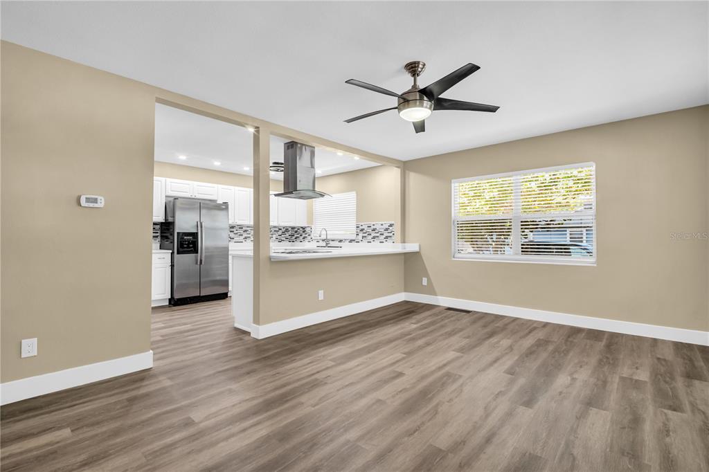 A living room with wood-look flooring opens to a kitchen featuring white cabinets and appliances — 1001 JASMINE WAY, CLEARWATER, FL