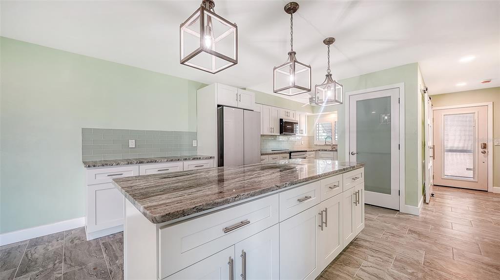 A kitchen features a large stone-topped island, white cabinetry, and light green walls — 4234 GULF OF MEXICO DRIVE UNIT M1, LONGBOAT KEY, FL