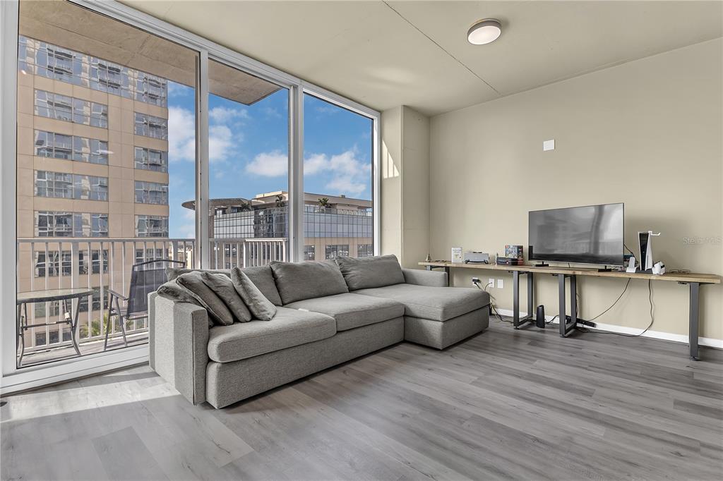 A living room features a grey sectional sofa, wood-look flooring, and floor-to-ceiling windows with balcony access — 155 S COURT AVENUE UNIT 1506, ORLANDO, FL