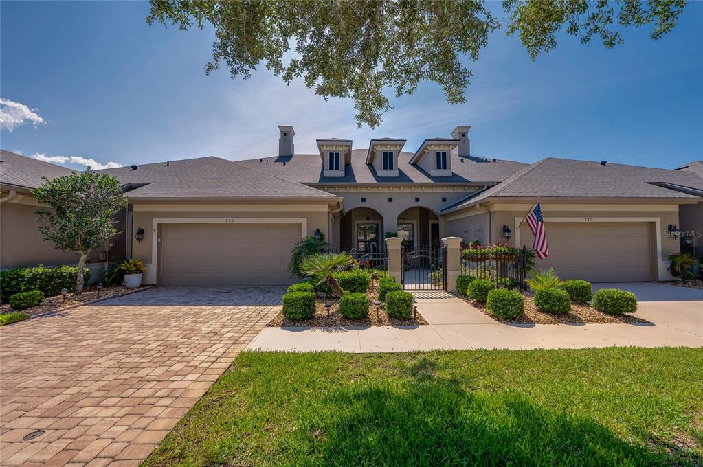 A single-story duplex with beige stucco walls, two garages, and a central gated courtyard — 735 COBBLESTONE DRIVE, ORMOND BEACH, FL
