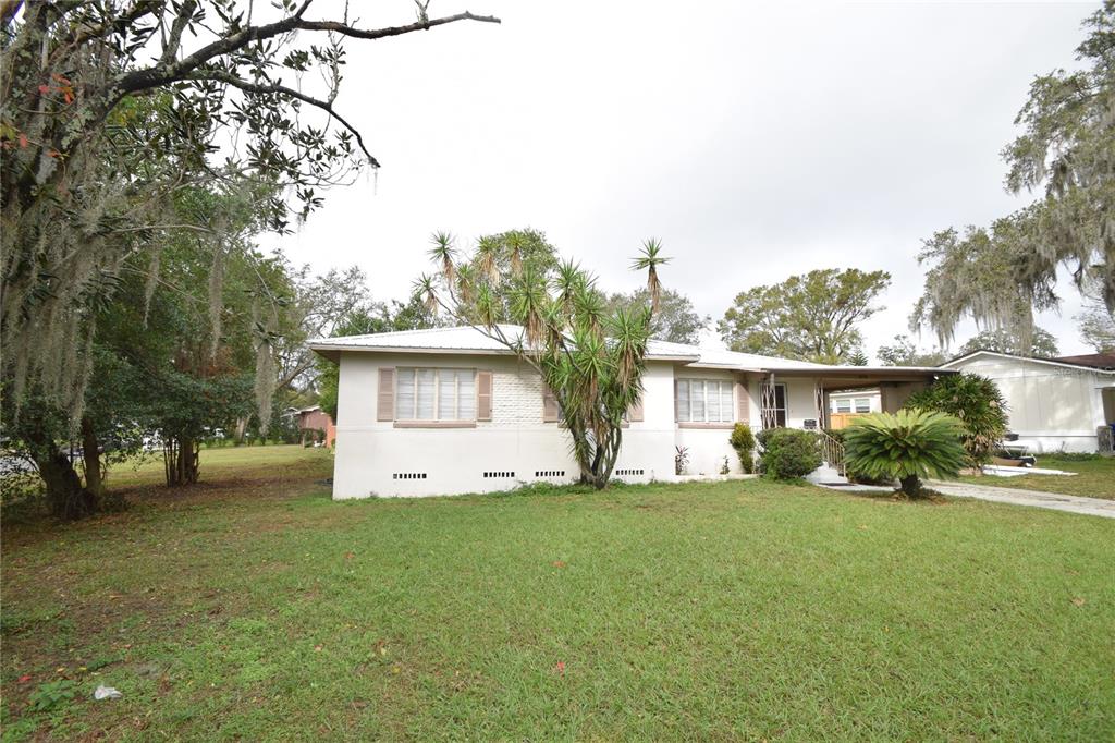 A single-story white house with a metal roof sits on a grassy lot with trees — 3115 BUCKINGHAM AVENUE, LAKELAND, FL