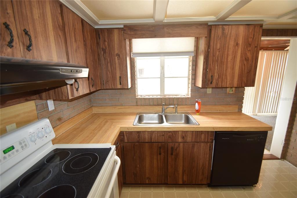 A kitchen features wood-grain cabinets, a laminate countertop, a double sink, and a black dishwasher — 3115 BUCKINGHAM AVENUE, LAKELAND, FL
