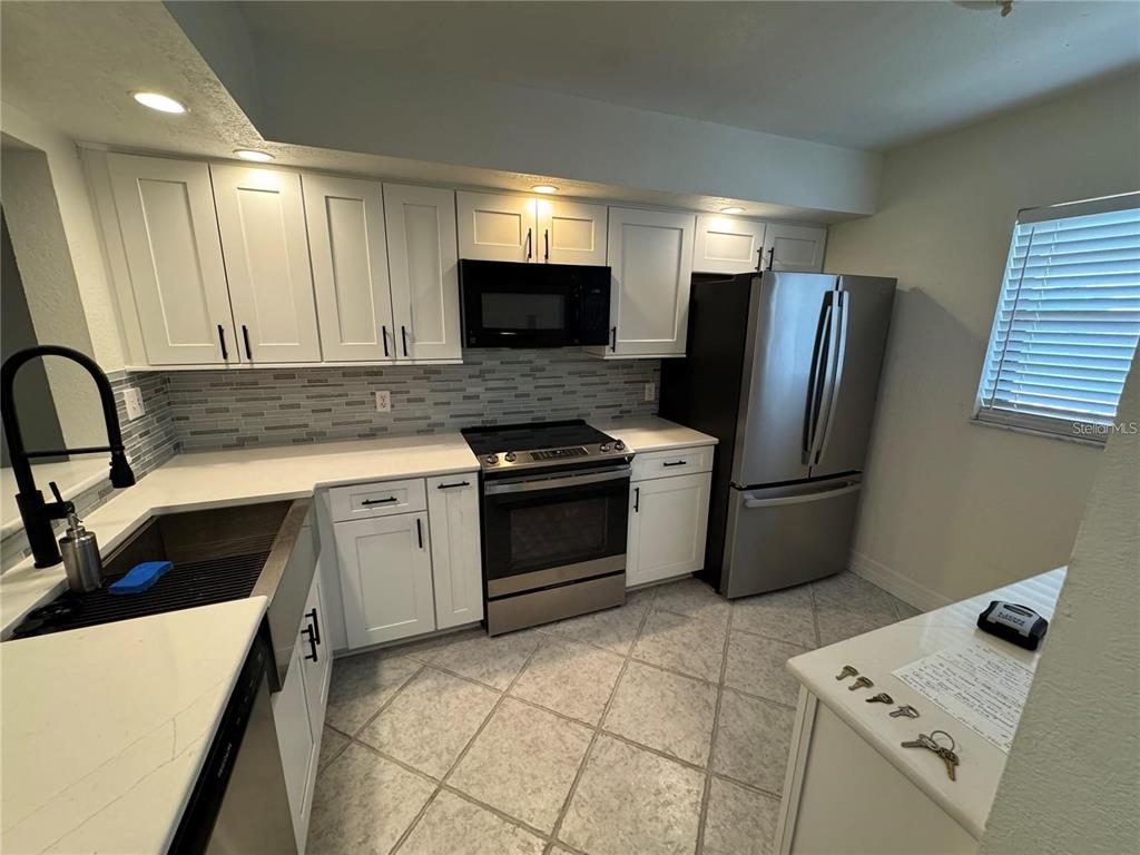 A kitchen features white cabinets, stainless steel appliances, a farmhouse sink, and tiled flooring — 2275 S MCCALL ROAD UNIT 201, ENGLEWOOD, FL