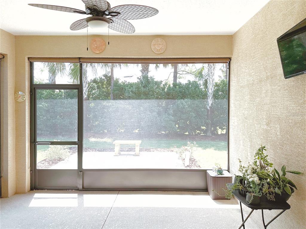 A screened-in patio features a ceiling fan, textured walls, a television, and a garden view — 7559 SW 97TH AVENUE, OCALA, FL