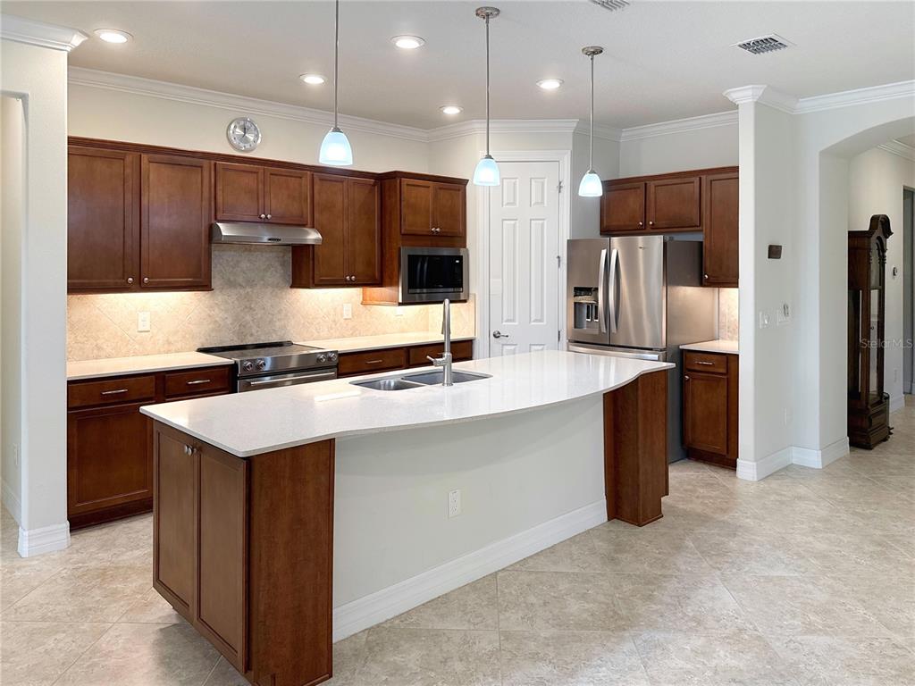 A kitchen features dark wood cabinets, a large white island, and stainless steel appliances — 7559 SW 97TH AVENUE, OCALA, FL